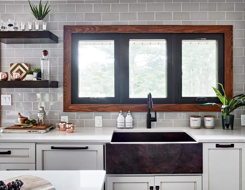 Rustik inredning av ett mellanstort vit vitt kök, med en rustik diskho, luckor med infälld panel, vita skåp, bänkskiva i glas, grått stänkskydd, stänkskydd i glaskakel, integrerade vitvaror, mellanmörkt trägolv, en köksö och brunt golv