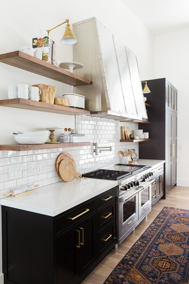 Klassisk inredning av ett linjärt kök med öppen planlösning, med en nedsänkt diskho, släta luckor, svarta skåp, vitt stänkskydd, stänkskydd i tunnelbanekakel, rostfria vitvaror, ljust trägolv och en köksö