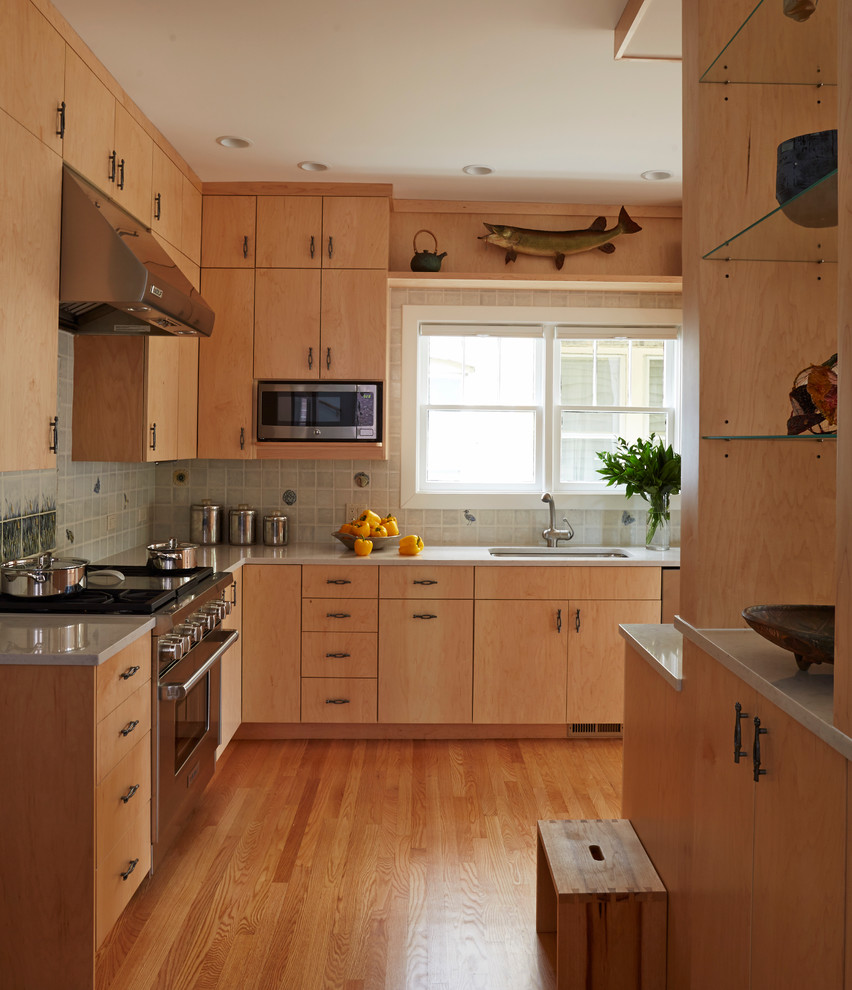 Inredning av ett modernt stort kök, med en enkel diskho, släta luckor, skåp i ljust trä, bänkskiva i glas, grått stänkskydd, stänkskydd i glaskakel, rostfria vitvaror, ljust trägolv, en köksö och brunt golv