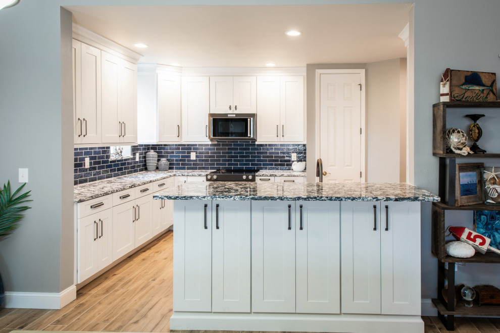 Inspiration for a mid-sized coastal l-shaped porcelain tile and beige floor eat-in kitchen remodel in Orlando with an undermount sink, shaker cabinets, white cabinets, quartz countertops, blue backsplash, ceramic backsplash, black appliances, a peninsula and blue countertops