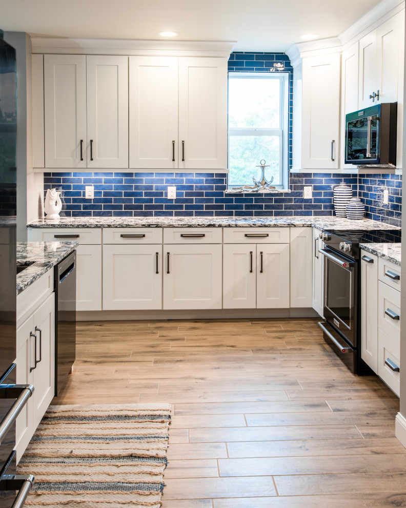 Maritim inredning av ett mellanstort blå blått kök, med en undermonterad diskho, skåp i shakerstil, vita skåp, bänkskiva i kvarts, blått stänkskydd, stänkskydd i keramik, svarta vitvaror, klinkergolv i porslin, en halv köksö och beiget golv