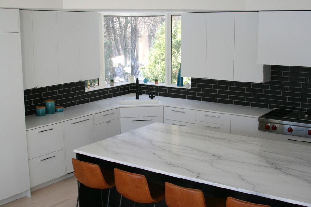 Ejemplo de cocinas en L minimalista grande con una isla, armarios con paneles lisos, salpicadero negro y suelo de madera clara