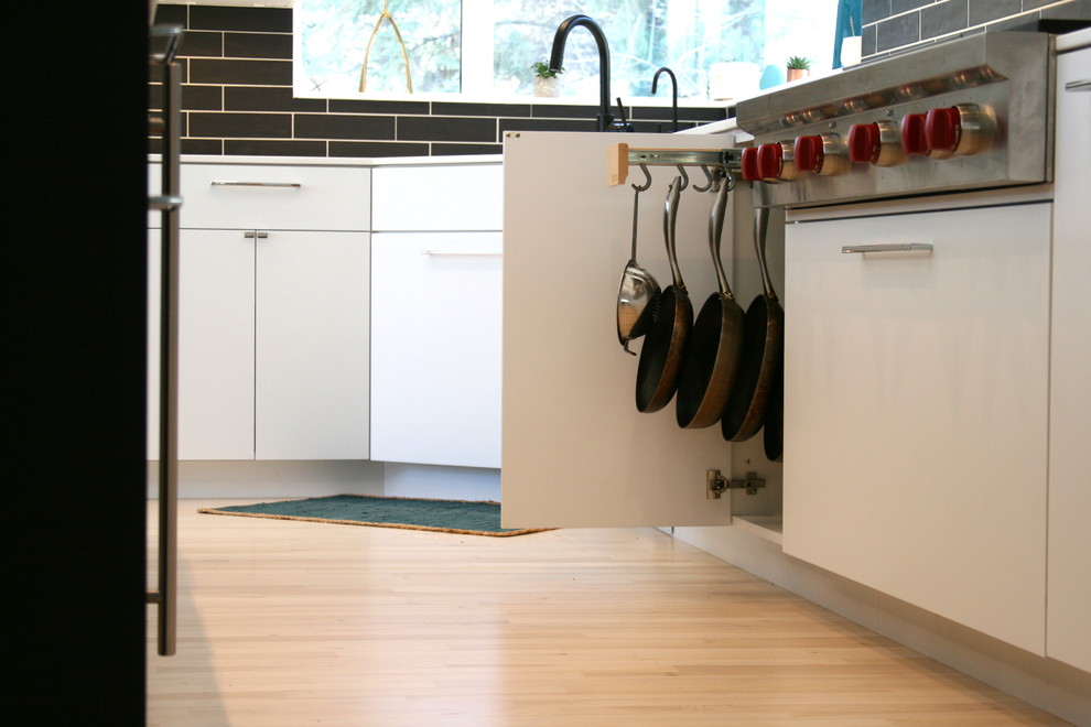 Imagen de cocinas en L moderna grande con una isla, armarios con paneles lisos, salpicadero negro y suelo de madera clara