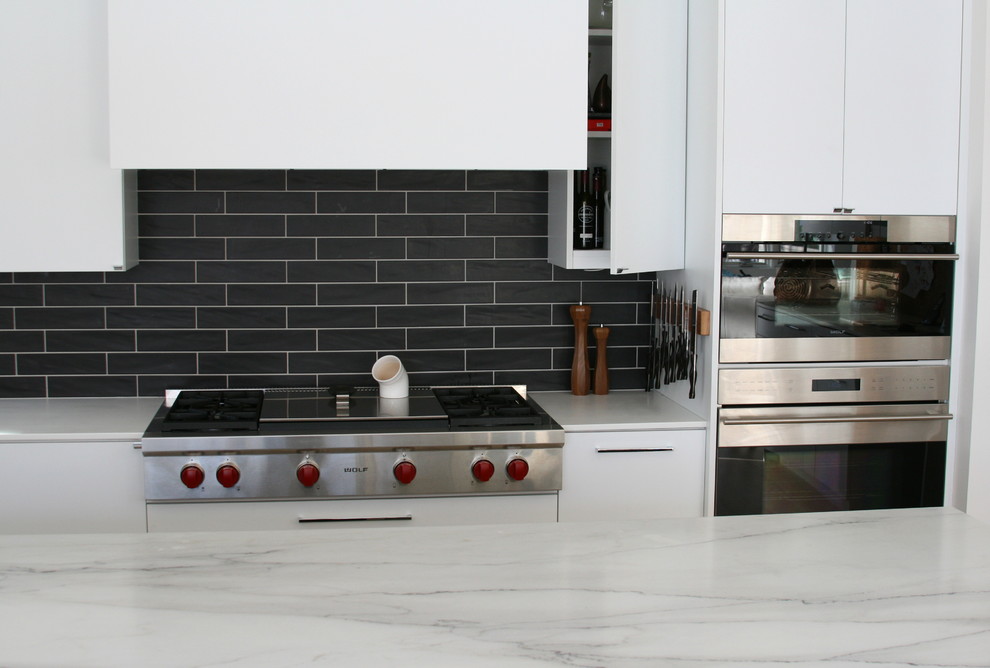 Foto på ett stort funkis l-kök, med en köksö, släta luckor, vita skåp och svart stänkskydd