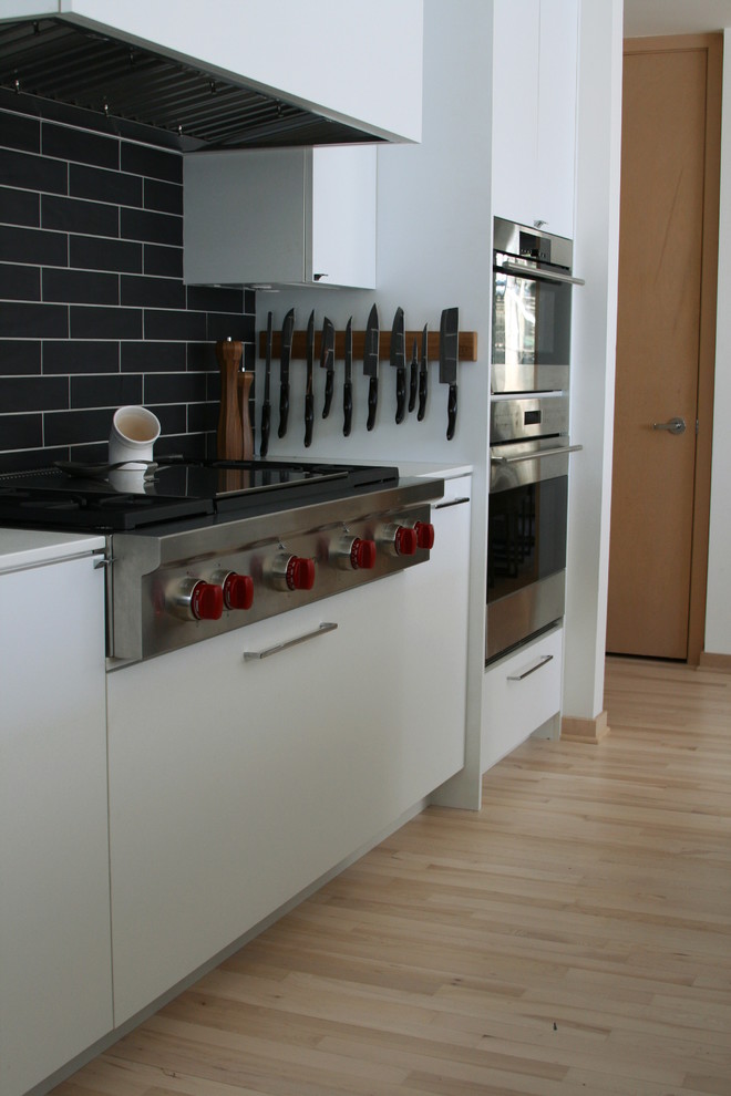 Modelo de cocinas en L minimalista grande con una isla, armarios con paneles lisos, puertas de armario blancas, electrodomésticos de acero inoxidable y suelo de madera clara