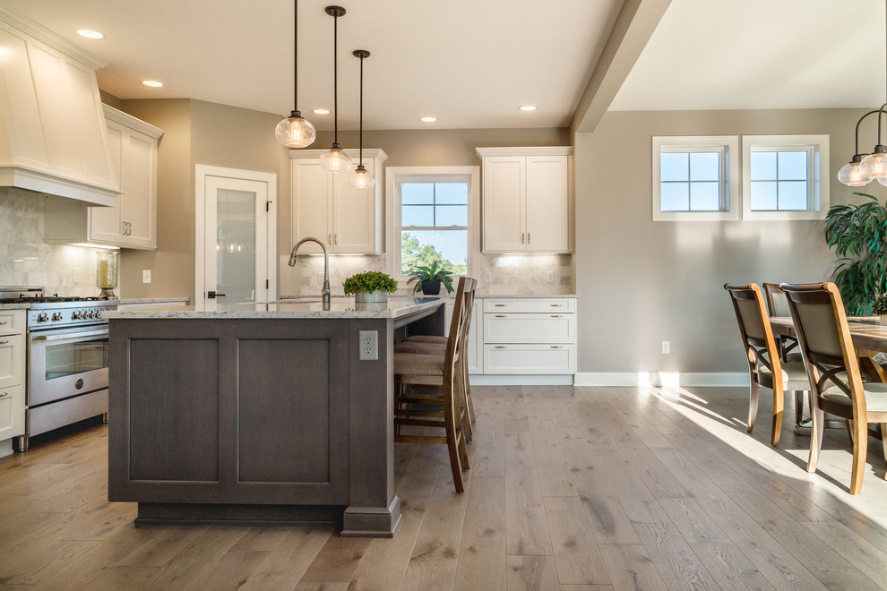 Inspiration for a large modern l-shaped light wood floor and gray floor eat-in kitchen remodel in New York with an undermount sink, white cabinets, white backsplash, marble backsplash, stainless steel appliances, an island and shaker cabinets