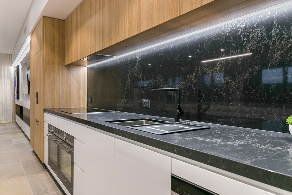 This is an example of a large modern galley open plan kitchen in Perth with a submerged sink, beaded cabinets, white cabinets, engineered stone countertops, black splashback, stone slab splashback, coloured appliances, marble flooring, an island, grey floors and black worktops.