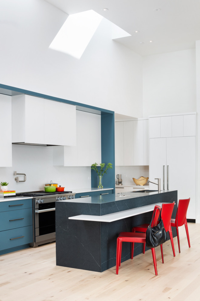 Cette image montre une cuisine design en L avec un évier encastré, un placard à porte plane, des portes de placard bleues, un électroménager en acier inoxydable, parquet clair, îlot, un sol beige et un plan de travail blanc.