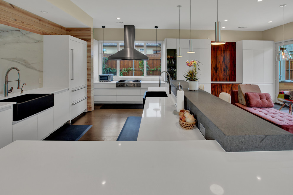 Moderne Küche mit Landhausspüle, flächenbündigen Schrankfronten, weißen Schränken, Quarzwerkstein-Arbeitsplatte, Rückwand aus Stein, Küchengeräten aus Edelstahl, braunem Holzboden, Kücheninsel, grauem Boden und grauer Arbeitsplatte in Dallas