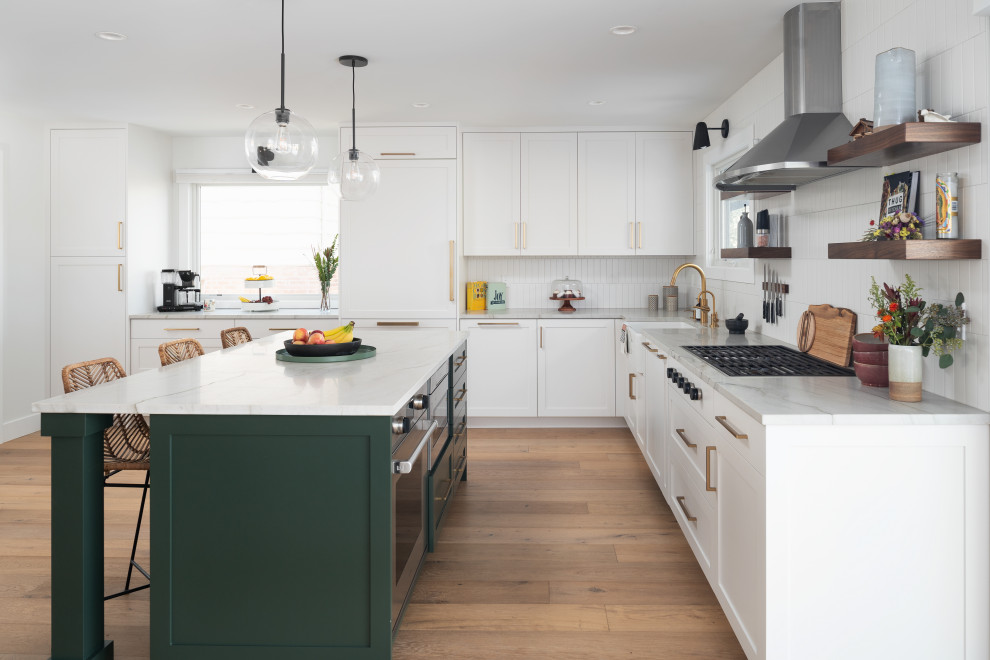 Minimalist l-shaped light wood floor open concept kitchen photo in Denver with a farmhouse sink, shaker cabinets, green cabinets, quartzite countertops, white backsplash, ceramic backsplash, stainless steel appliances, an island and white countertops