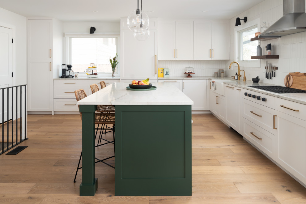 Modern inredning av ett vit vitt kök, med en rustik diskho, skåp i shakerstil, gröna skåp, bänkskiva i kvartsit, vitt stänkskydd, stänkskydd i keramik, rostfria vitvaror, ljust trägolv och en köksö