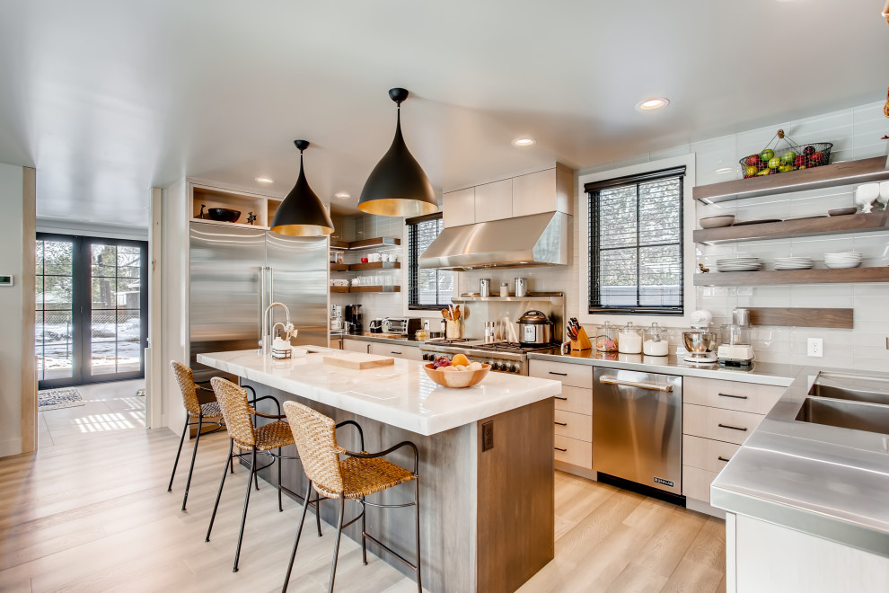 Inspiration for a contemporary u-shaped beige floor kitchen remodel in Denver with an integrated sink, flat-panel cabinets, beige cabinets, stainless steel countertops, white backsplash, stainless steel appliances and an island