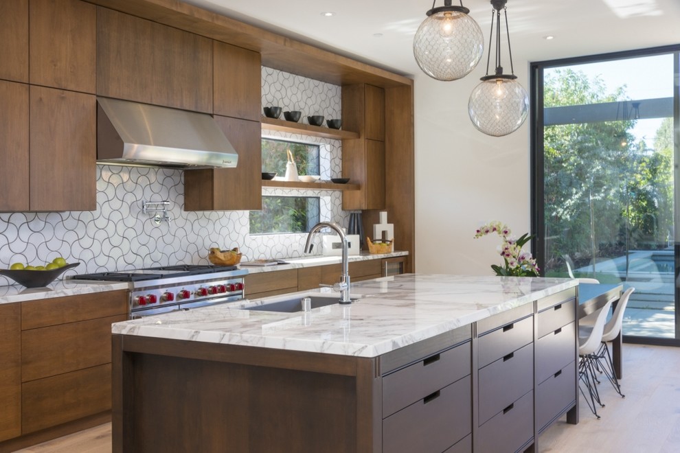 Foto de cocina actual con fregadero bajoencimera, armarios con paneles lisos, puertas de armario de madera en tonos medios, encimera de mármol, salpicadero blanco, salpicadero de azulejos de cerámica, electrodomésticos de acero inoxidable, suelo de madera clara y una isla