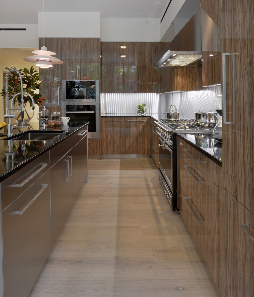 Bild på ett stort funkis kök, med en undermonterad diskho, släta luckor, skåp i mellenmörkt trä, stänkskydd med metallisk yta, rostfria vitvaror, ljust trägolv och en köksö