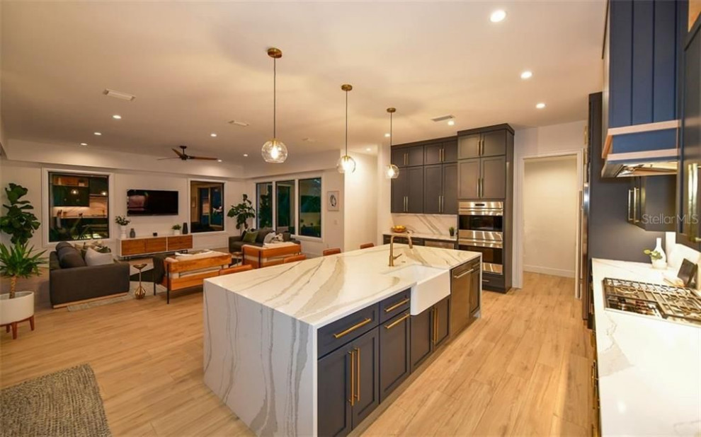 Foto di una grande cucina minimalista con ante blu, top in marmo, elettrodomestici in acciaio inossidabile, parquet chiaro e top multicolore