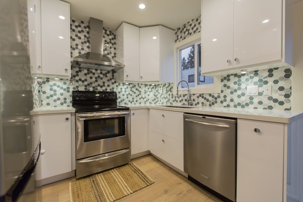 Moderne Wohnküche in U-Form mit Unterbauwaschbecken, flächenbündigen Schrankfronten, weißen Schränken, Küchenrückwand in Grün, Glasrückwand, Küchengeräten aus Edelstahl, Vinylboden, Kücheninsel und braunem Boden in Vancouver