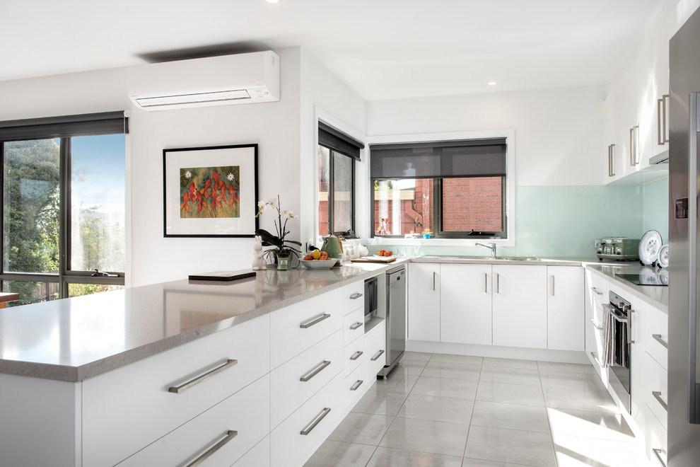 Inspiration for a modern u-shaped ceramic tile and gray floor open concept kitchen remodel in Melbourne with a double-bowl sink, flat-panel cabinets, white cabinets, quartz countertops, green backsplash, glass sheet backsplash and stainless steel appliances