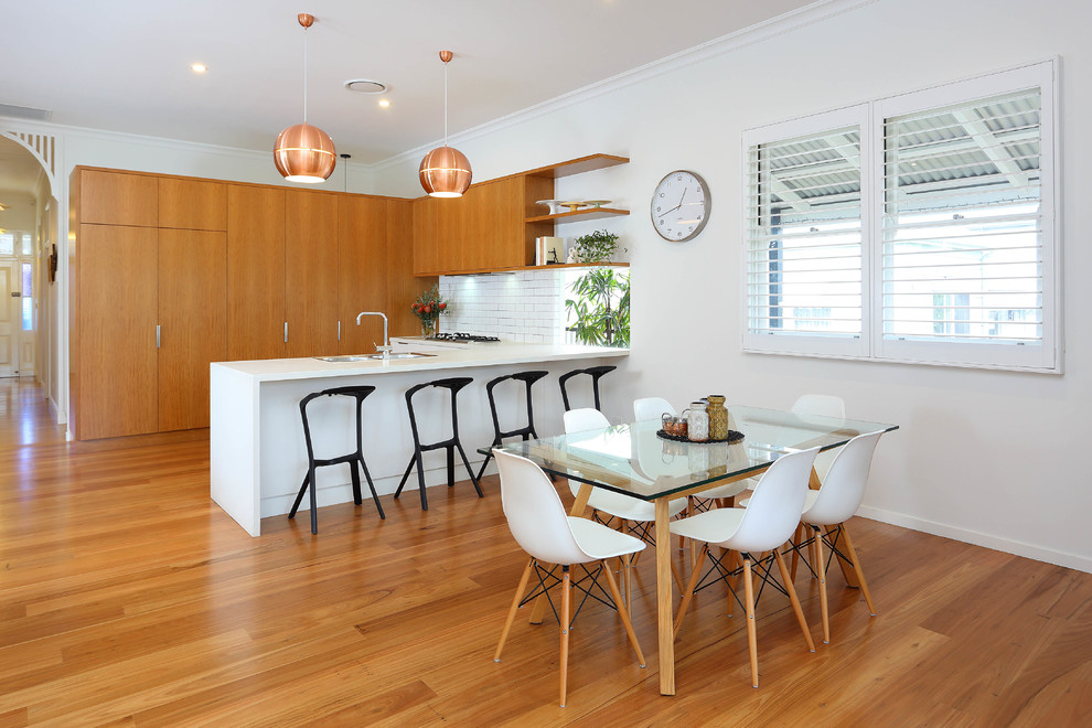 Mittelgroße Moderne Wohnküche in U-Form mit Einbauwaschbecken, flächenbündigen Schrankfronten, hellbraunen Holzschränken, Mineralwerkstoff-Arbeitsplatte, Küchenrückwand in Weiß, Rückwand aus Keramikfliesen und braunem Holzboden in Brisbane