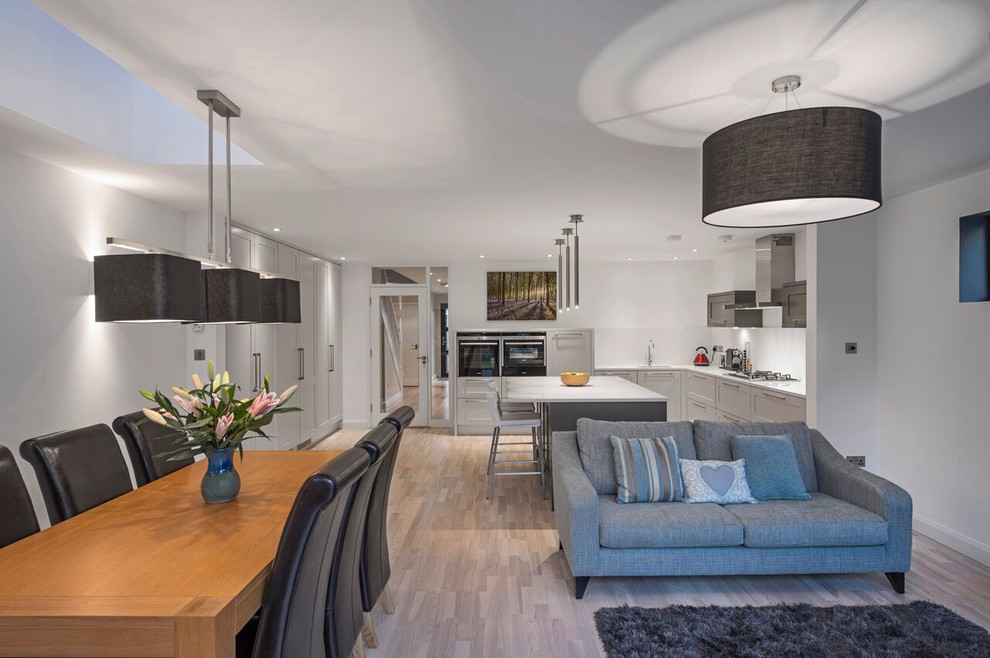 Design ideas for a large contemporary l-shaped open plan kitchen in Dublin with a breakfast bar, shaker cabinets, grey cabinets, an integrated sink, laminate countertops, white splashback, ceramic splashback, integrated appliances and light hardwood flooring.