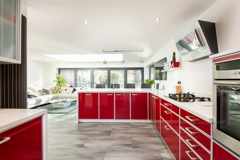 На фото: угловая кухня-гостиная среднего размера в стиле неоклассика (современная классика) с красными фасадами, мраморной столешницей, плоскими фасадами, техникой из нержавеющей стали, серым полом и бежевой столешницей