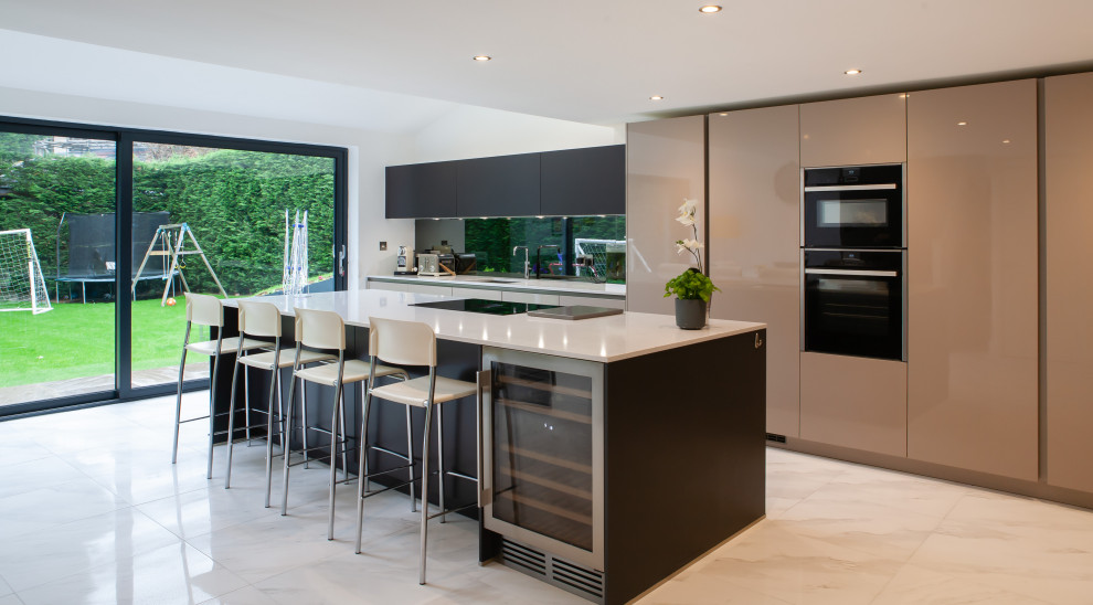 Inspiration for a contemporary l-shaped kitchen/diner in Other with a submerged sink, flat-panel cabinets, beige cabinets, black splashback, glass sheet splashback, integrated appliances, an island, multi-coloured floors and white worktops.