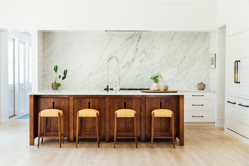 Inredning av ett skandinaviskt kök, med vita skåp, vitt stänkskydd, stänkskydd i marmor, ljust trägolv, en köksö och beiget golv