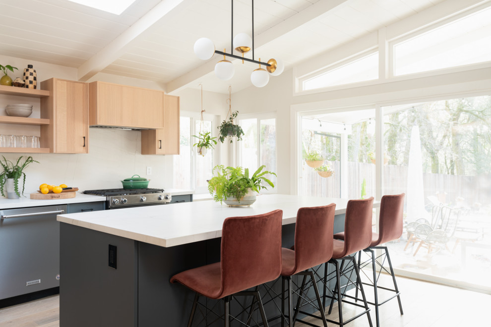 Inspiration for a midcentury kitchen in San Francisco with flat-panel cabinets, light wood cabinets, white splashback, stainless steel appliances, light hardwood flooring, an island, white worktops, engineered stone countertops, marble splashback and a vaulted ceiling.