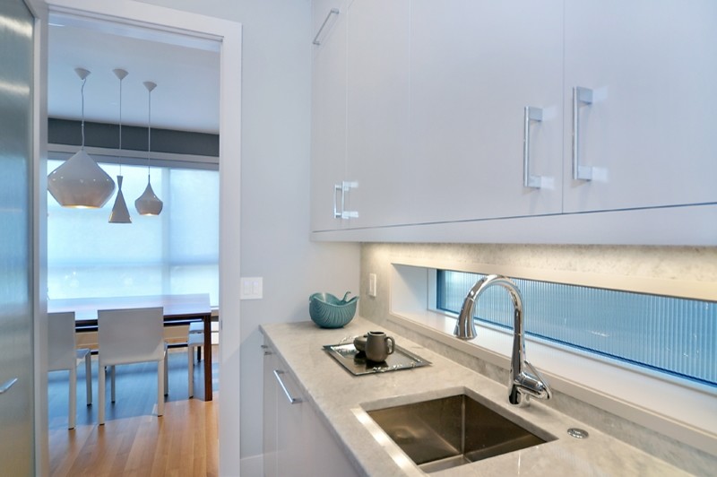 Moderne Küche mit Unterbauwaschbecken, flächenbündigen Schrankfronten, weißen Schränken, Granit-Arbeitsplatte und Küchenrückwand in Weiß in Calgary