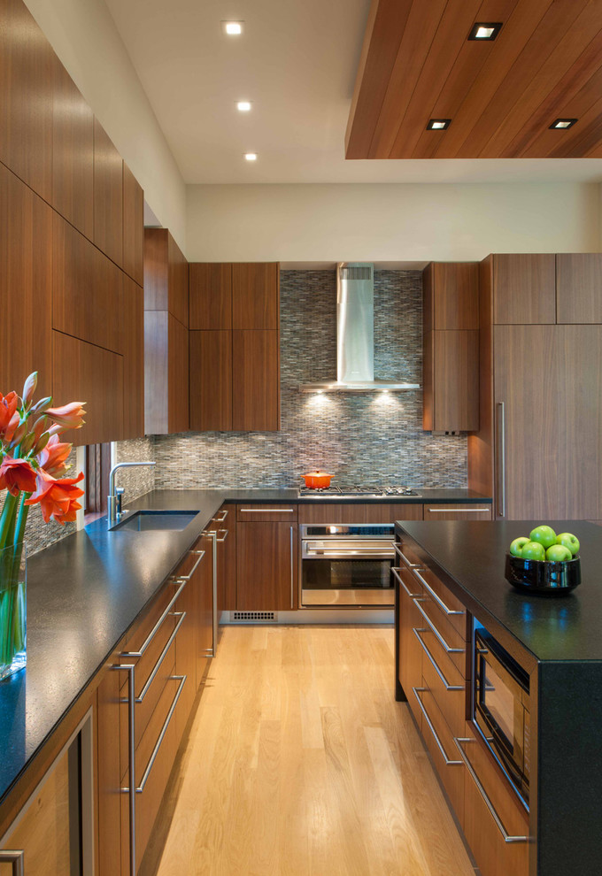 Inspiration for a contemporary u-shaped medium tone wood floor kitchen remodel in DC Metro with an undermount sink, flat-panel cabinets, granite countertops, mosaic tile backsplash, paneled appliances, an island, dark wood cabinets and gray backsplash
