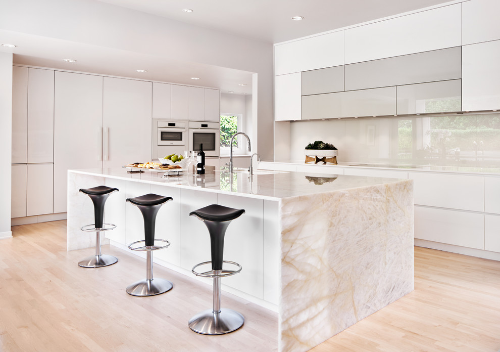 Inspiration for a large contemporary l-shaped kitchen/diner in Dallas with a submerged sink, flat-panel cabinets, white cabinets, white splashback, glass sheet splashback, light hardwood flooring, an island, beige floors, beige worktops, onyx worktops, white appliances and a vaulted ceiling.