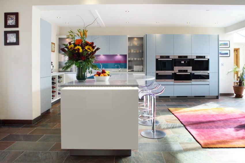Photo of a large contemporary l-shaped kitchen/diner in Buckinghamshire with flat-panel cabinets, blue cabinets, granite worktops, blue splashback, glass tiled splashback, an island and stainless steel appliances.