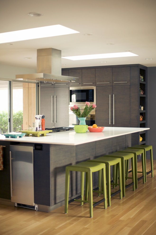 Стильный дизайн: кухня-гостиная среднего размера в стиле модернизм с плоскими фасадами, серыми фасадами, техникой из нержавеющей стали, светлым паркетным полом и островом - последний тренд