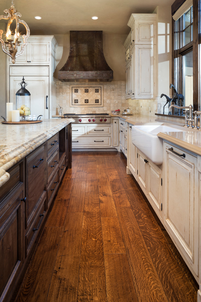 Inspiration for an expansive rustic u-shaped kitchen in Minneapolis with a belfast sink, raised-panel cabinets, distressed cabinets, granite worktops, beige splashback, stone tiled splashback, stainless steel appliances, an island, dark hardwood flooring and brown floors.