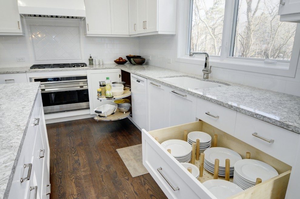 Foto de cocina actual con fregadero de un seno, armarios estilo shaker, puertas de armario blancas, encimera de granito, salpicadero blanco, salpicadero de azulejos tipo metro, electrodomésticos de acero inoxidable, suelo de madera oscura y una isla