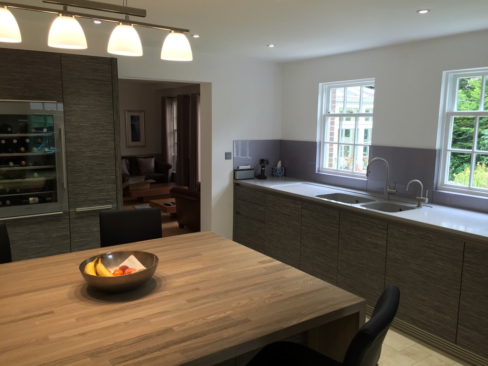 Large contemporary kitchen/diner in Oxfordshire with a single-bowl sink, flat-panel cabinets, light wood cabinets, engineered stone countertops, multi-coloured splashback, glass tiled splashback, stainless steel appliances, ceramic flooring, an island and beige floors.