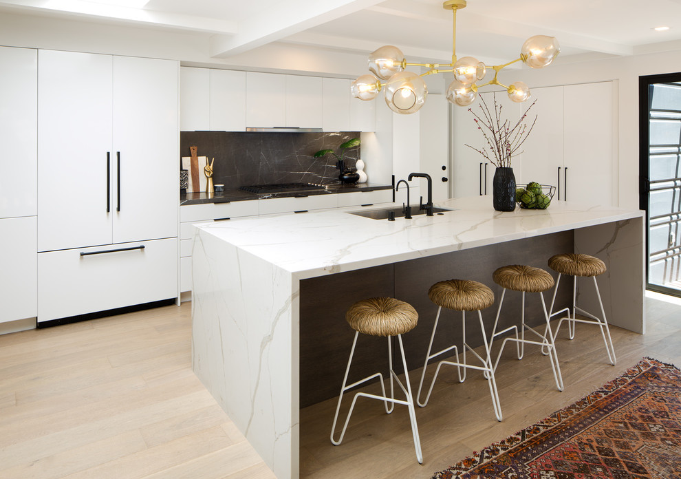 Inspiration for a midcentury l-shaped kitchen in San Diego with a submerged sink, flat-panel cabinets, white cabinets, black splashback, marble splashback, integrated appliances, light hardwood flooring, an island, beige floors and white worktops.