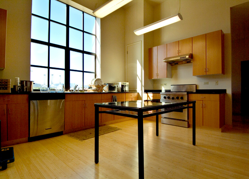 Exempel på ett modernt kök, med en undermonterad diskho, släta luckor, skåp i mellenmörkt trä, bänkskiva i rostfritt stål, beige stänkskydd, rostfria vitvaror, betonggolv och en köksö