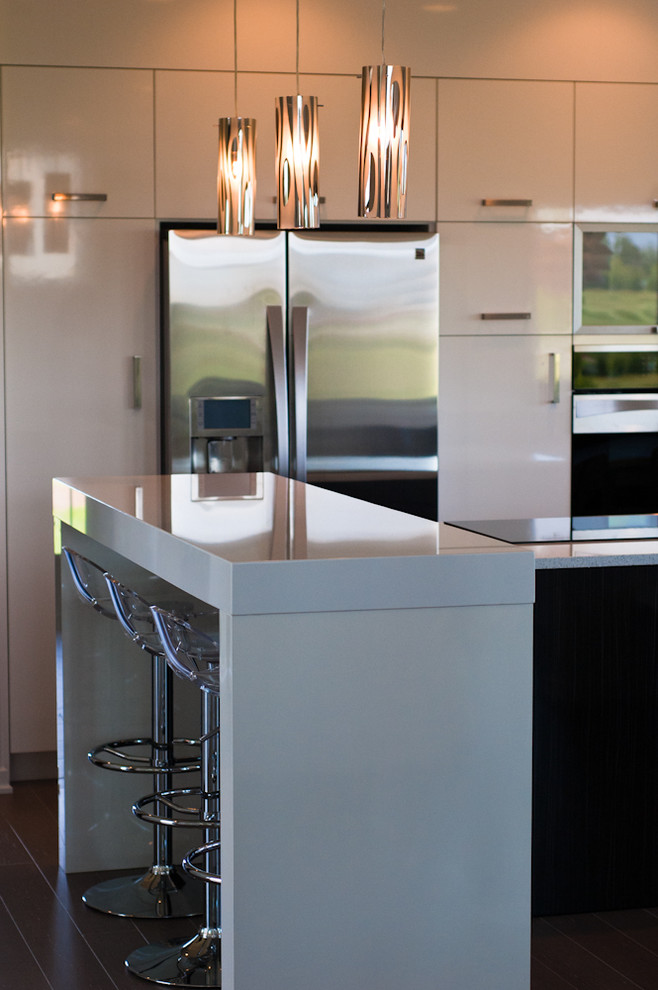 This is an example of a small modern l-shaped kitchen/diner in Grand Rapids with flat-panel cabinets, white cabinets, engineered stone countertops, stainless steel appliances, dark hardwood flooring, multiple islands, brown floors, white worktops and a submerged sink.
