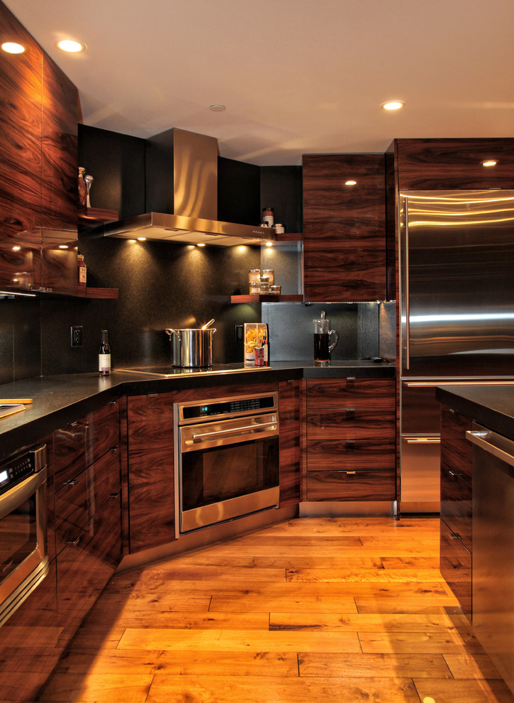 Bild på ett avskilt, stort funkis svart svart l-kök, med släta luckor, skåp i mörkt trä, svart stänkskydd, rostfria vitvaror, mellanmörkt trägolv, en undermonterad diskho, granitbänkskiva, stänkskydd i sten, en köksö och brunt golv