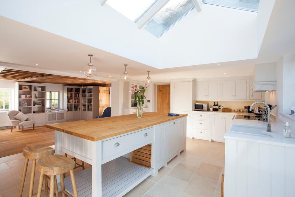 This is an example of a large farmhouse l-shaped open plan kitchen in Kent with a belfast sink, shaker cabinets, grey cabinets, quartz worktops, white splashback, stone slab splashback, stainless steel appliances, limestone flooring and an island.