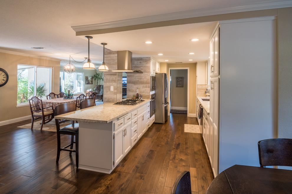 Example of a mid-sized classic galley medium tone wood floor and brown floor open concept kitchen design in Sacramento with an undermount sink, recessed-panel cabinets, white cabinets, granite countertops, gray backsplash, stainless steel appliances, a peninsula and gray countertops