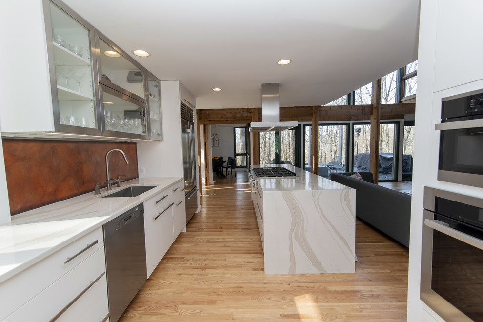 Design ideas for a large modern galley kitchen/diner in Baltimore with a submerged sink, flat-panel cabinets, white cabinets, engineered stone countertops, stainless steel appliances, medium hardwood flooring, an island and white worktops.