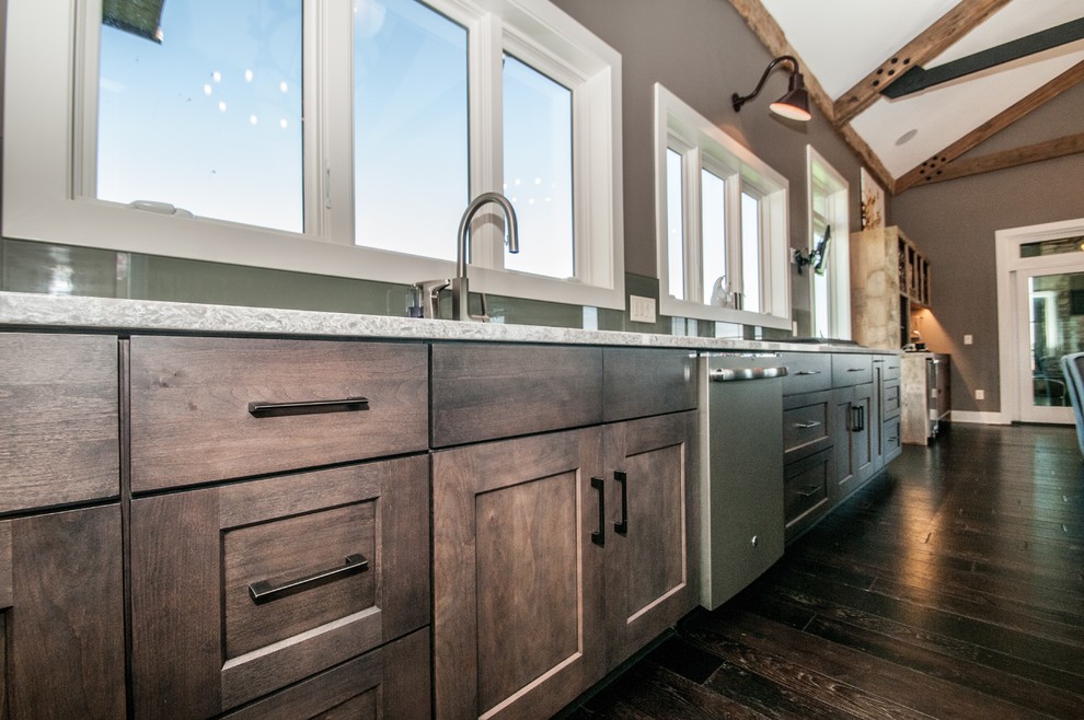 Inspiration for a large rustic kitchen/diner in Other with a submerged sink, flat-panel cabinets, medium wood cabinets, engineered stone countertops, green splashback, glass sheet splashback, stainless steel appliances, dark hardwood flooring, an island and brown floors.