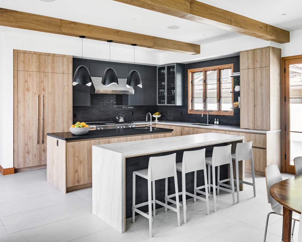 This is an example of a medium sized contemporary u-shaped kitchen/diner in Orange County with a submerged sink, flat-panel cabinets, light wood cabinets, quartz worktops, black splashback, stone tiled splashback, integrated appliances, cement flooring, multiple islands, grey floors and white worktops.