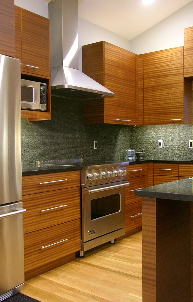 Inredning av ett modernt kök, med en integrerad diskho, släta luckor, skåp i mellenmörkt trä, granitbänkskiva, grått stänkskydd, stänkskydd i stenkakel och rostfria vitvaror