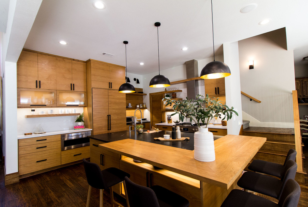 Bild på ett stort minimalistiskt svart svart kök och matrum, med släta luckor, skåp i ljust trä, granitbänkskiva, vitt stänkskydd, stänkskydd i tunnelbanekakel, rostfria vitvaror, mörkt trägolv, en köksö och brunt golv