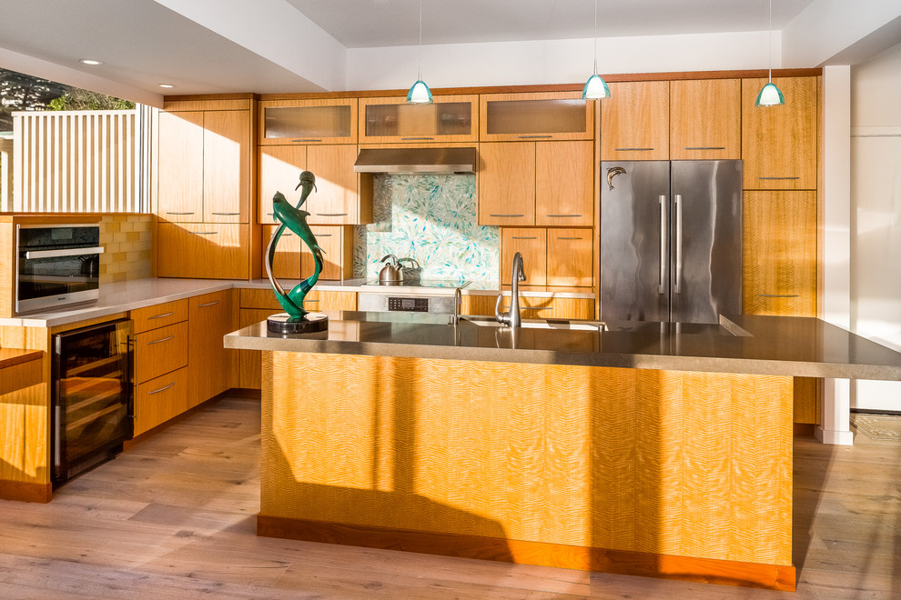 Example of a mid-sized beach style l-shaped medium tone wood floor and beige floor open concept kitchen design in Other with an undermount sink, flat-panel cabinets, light wood cabinets, quartz countertops, blue backsplash, glass tile backsplash, stainless steel appliances and an island