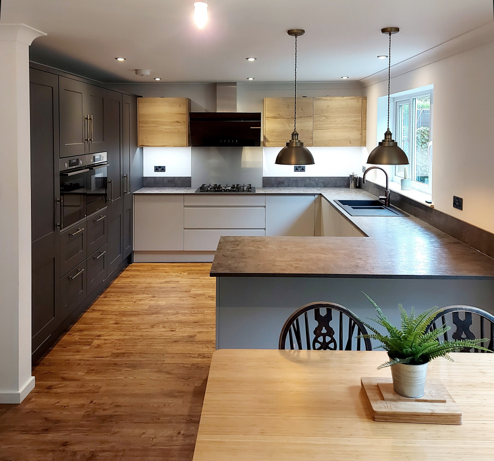 Idéer för mellanstora eklektiska grått kök, med en dubbel diskho, luckor med infälld panel, vita skåp, laminatbänkskiva, grått stänkskydd, glaspanel som stänkskydd, svarta vitvaror, mellanmörkt trägolv, en halv köksö och brunt golv