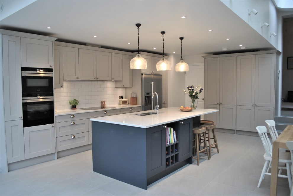 Minimalist porcelain tile and gray floor eat-in kitchen photo in London with a drop-in sink, shaker cabinets, gray cabinets, quartzite countertops, white backsplash, subway tile backsplash, stainless steel appliances, an island and white countertops