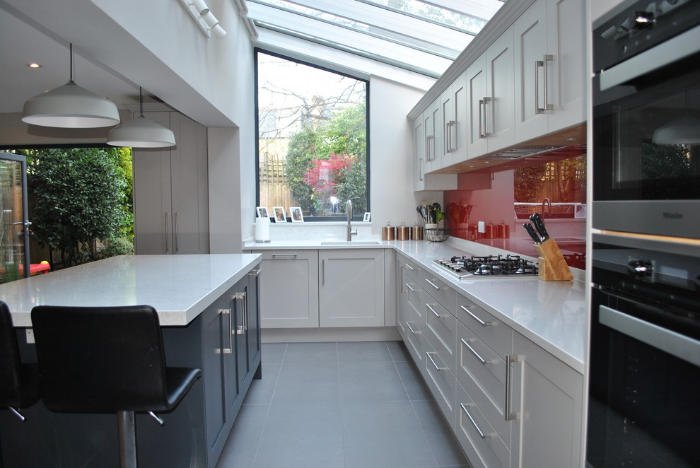 Exempel på ett stort modernt vit vitt kök, med en enkel diskho, skåp i shakerstil, grå skåp, bänkskiva i kvartsit, rött stänkskydd, glaspanel som stänkskydd, svarta vitvaror, klinkergolv i porslin, en köksö och grått golv